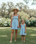 Woman and young girl in matching blue dresses standing in a garden.